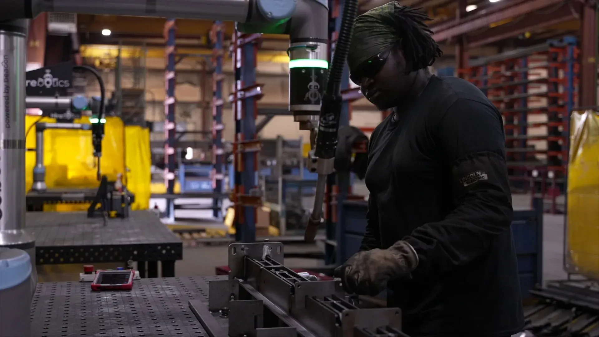 Welder loading a fixtured part beside a Beacon cobot welder