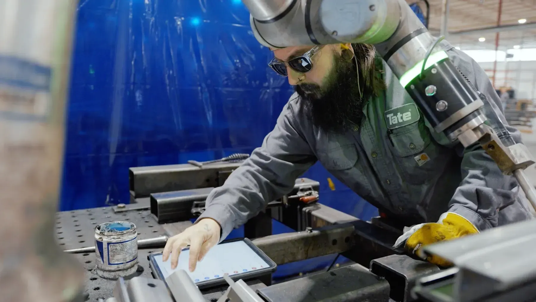 Operator in a Tate vest setting up a cobot weld job on a tablet