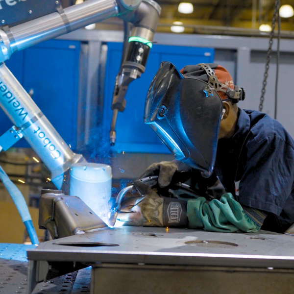 Huncilman lead welder with weld mask next to Hirebotics Cobot Welder